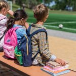 Children with backpacks enjoy after-school program activities outside.