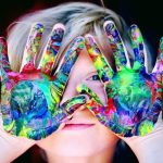 A child holding their hands up with paint on their hands